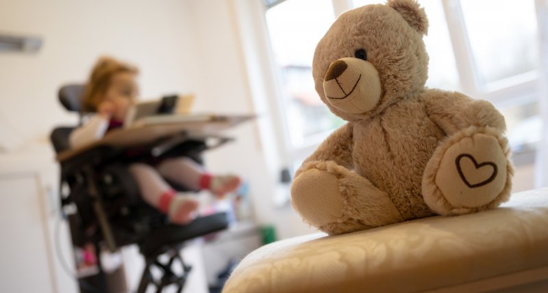 Backnang Ein Teddybaer sitzt vor einem Kind in einem Therapiestuhl das an spinaler Muskelatrophie SMA leidet